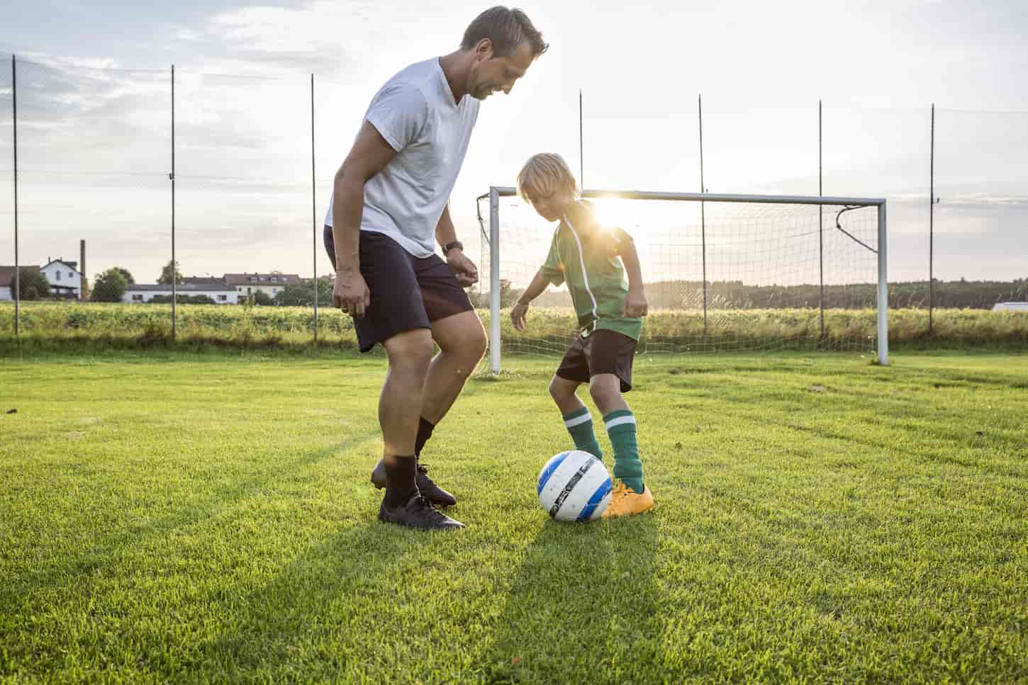 An image of a Coach and young football player on football ground at sunset.