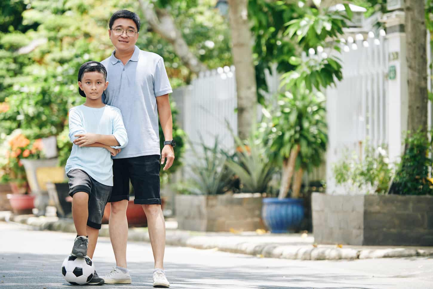 An image of a Smiling father posing with his preteen son after they played soccer together in the street.