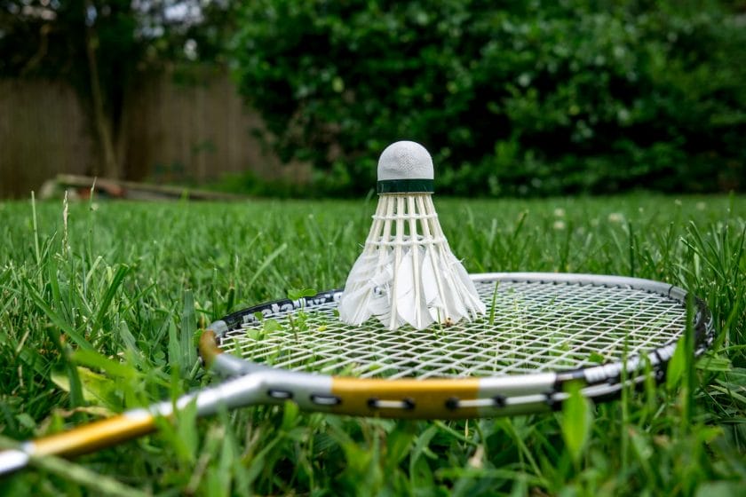 An image of a badminton racket and a shuttlecock in the backyard green lawn.