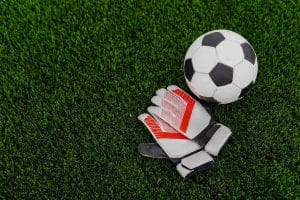 An image of a Soccer ball and goalkeeper gloves on football field.