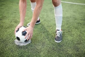 An image of a young player putting a soccer ball on a special area on a green field before the game.