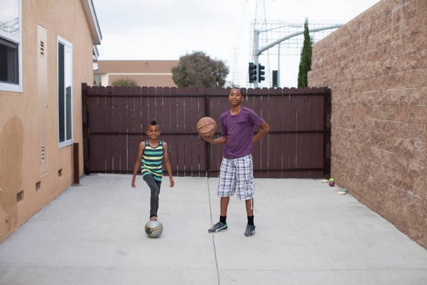 An image of two boys in a yard with a basketball and football.