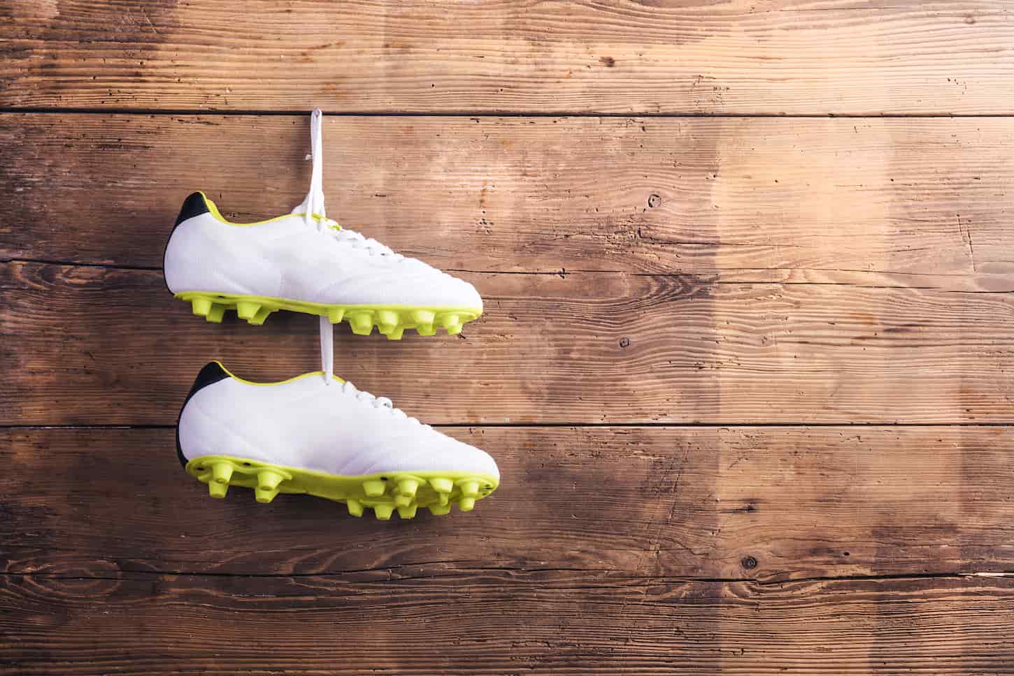 An image of a Pair of football shoes hanging on a nail on a wooden fence background.