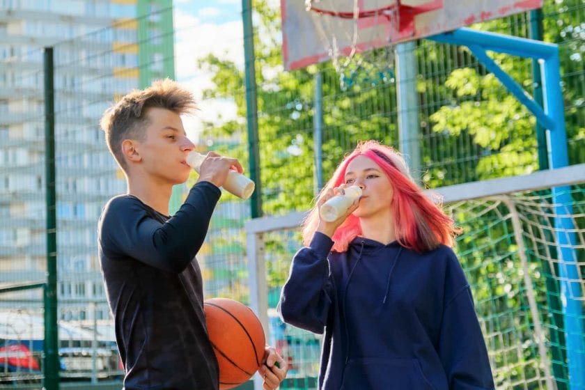An image of a couple of guys and a teenage girl drinking milk and healthy yogurt from a bottle on a sports city basketball court.