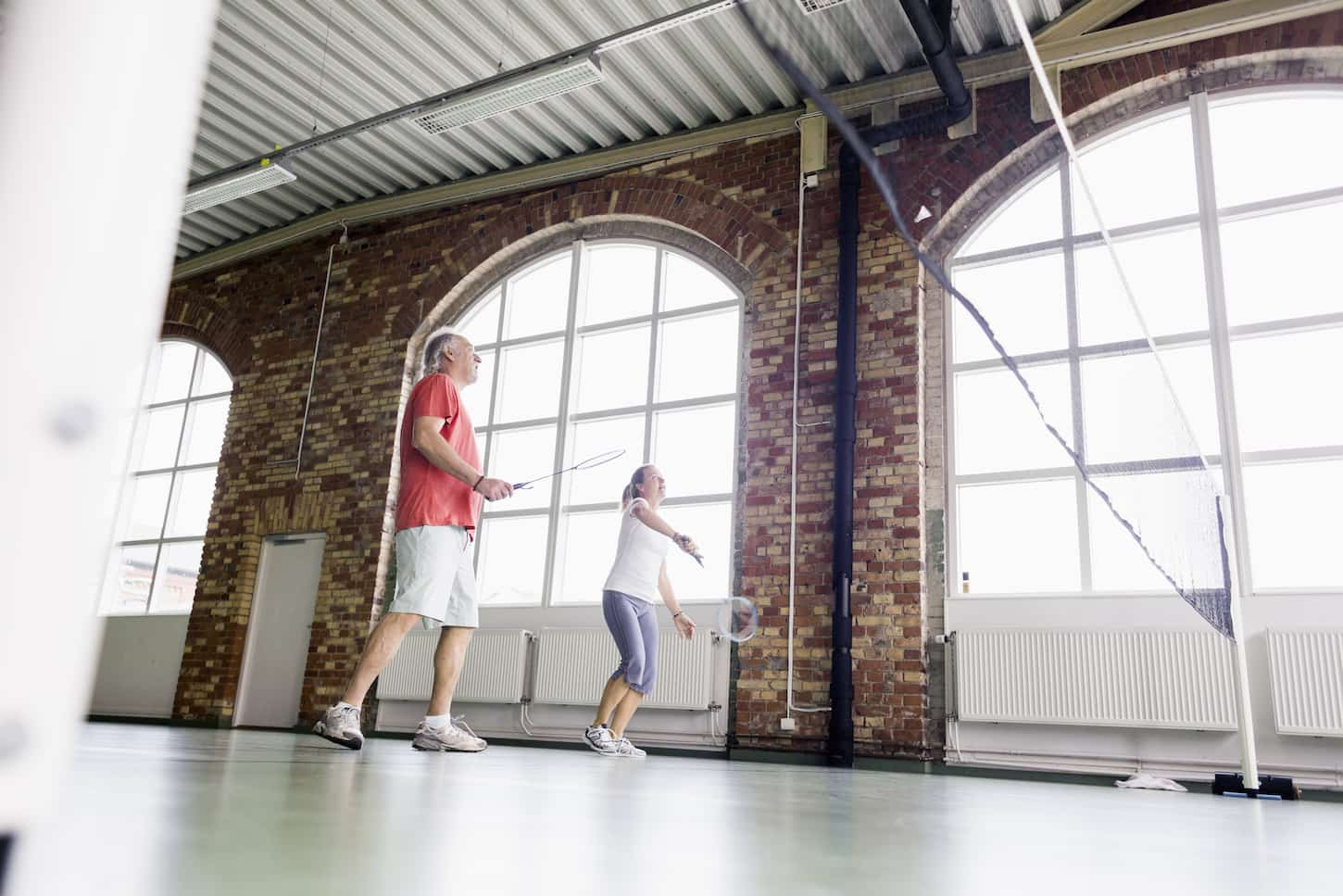 An image of a Man and woman playing badminton in a health club.