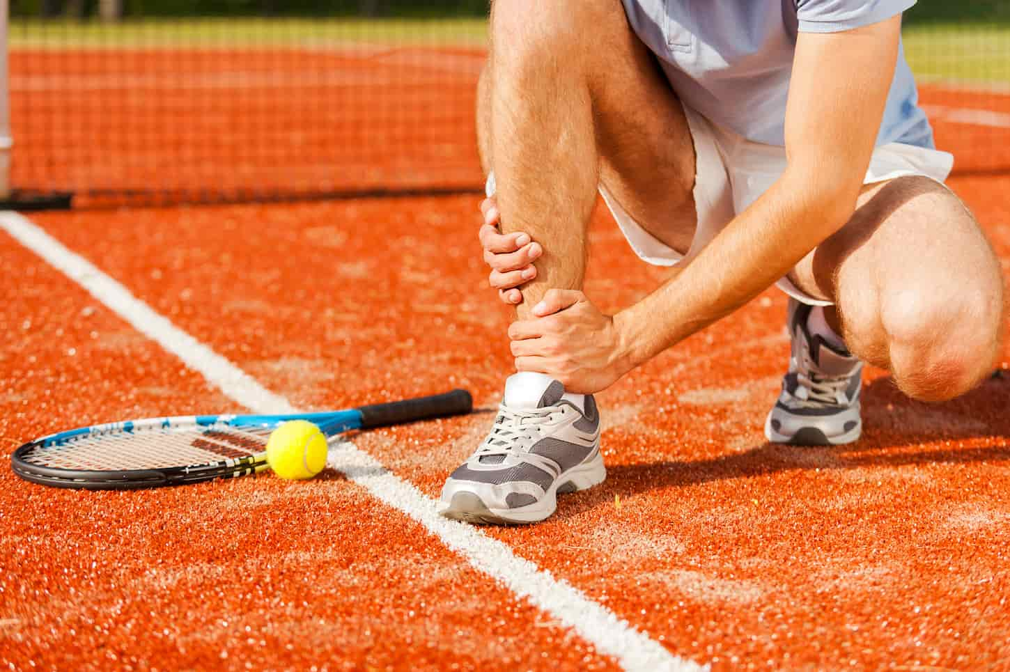 An image of a tennis player touching his leg while sitting on the tennis court.