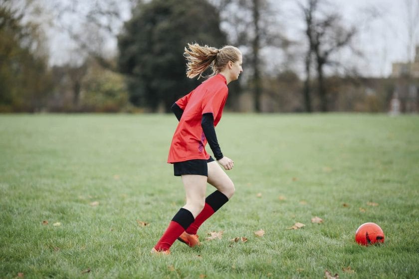 An image of a Teenage female soccer player practicing with the soccer ball in park.