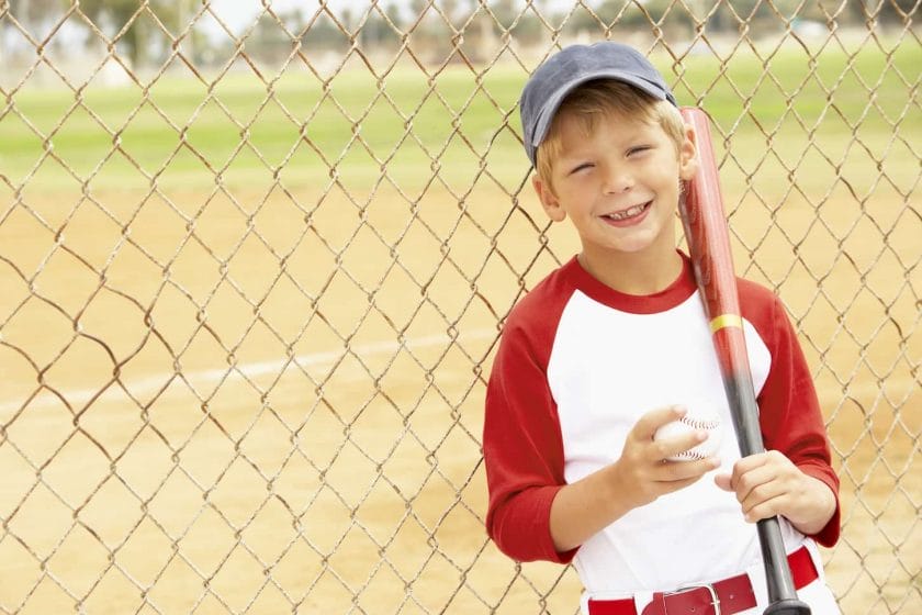 An image of a Young Boy Playing Baseball and smiling to the camera.