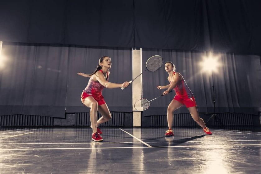 An image of two young women playing badminton over a gym background. Concept game in a pair.
