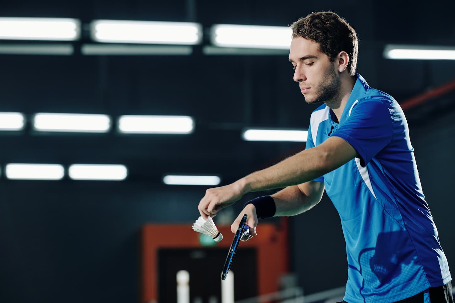 An image of a Professional young serious badminton player serving shuttlecock when playing in a gymnasium.