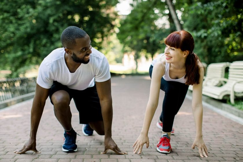 An image of a Multiethnic couple in sports clothes on starting line preparing to run in the park, smiling and looking at each other. Healthy fit and sportive couple starting position ready for running.