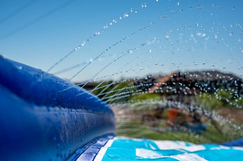An image of Selective focus on water spray shooting across a slip-and-slide perched on the top of a hill.