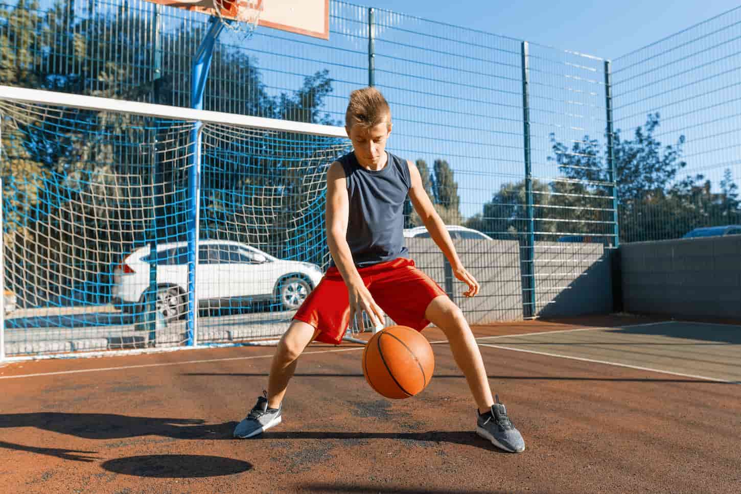 An image of a Caucasian teenage boy street basketball player with a ball on an outdoor city basketball court.