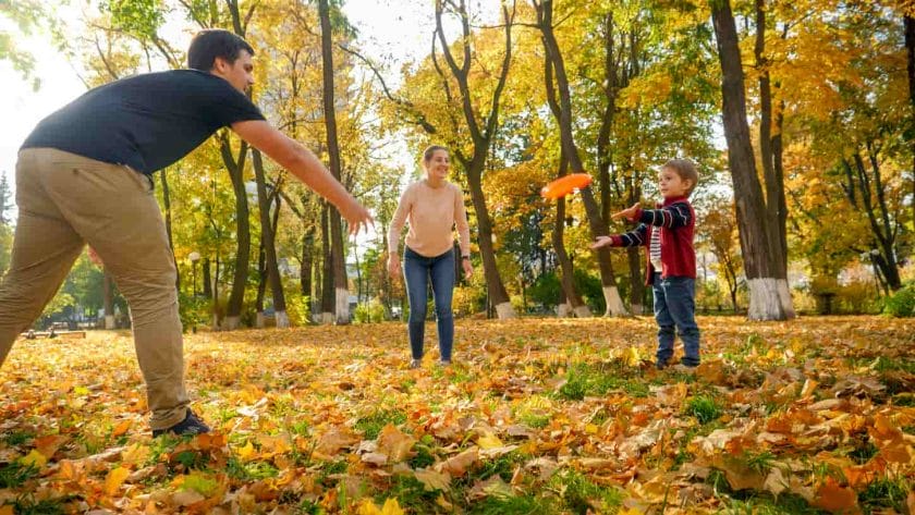 An image of a happy, smiling family playing with a frisbee in an autumn park.