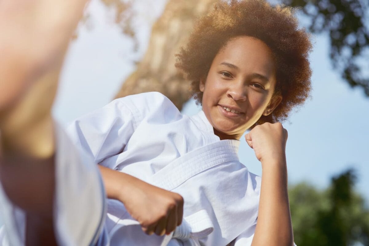 An image of an Adorable female child in karate kimono looking at the camera and smiling while doing a fighting stance.