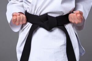An image of hands of karate girl in white kimono and black belt training karate over gray background.