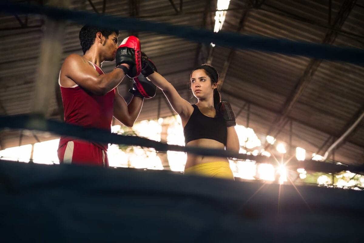 An image of a Young woman exercising with a trainer at a boxing area and a self-defense lesson.