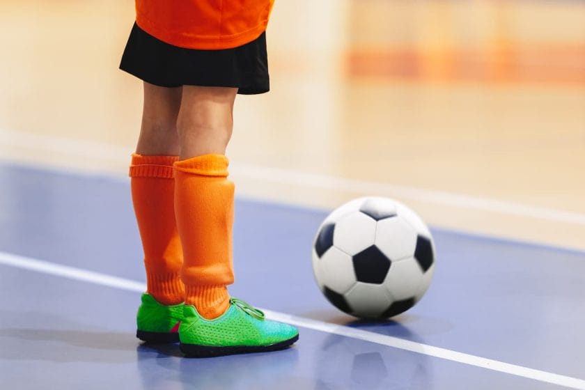An image of a Football futsal player with a ball. Futsal floor and players in training. Sports background. Indoor soccer sports hall. Youth futsal league. Indoor football classic ball.