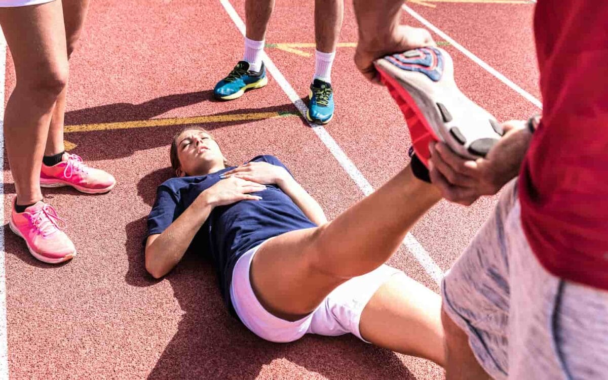 An image of a Female athlete injured on athletic run training. A Male coach taking care of an athlete having fatigue cramps.