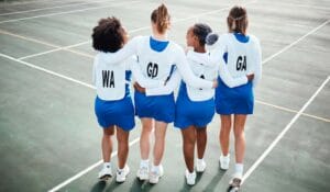 An image of four teenage athletes on a Netball team practicing in the court.