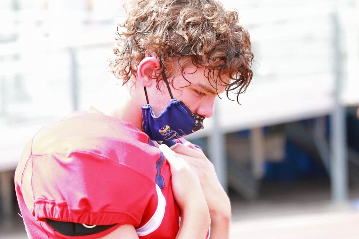 An image of a Young athlete deep in thought on the sideline during a football game.