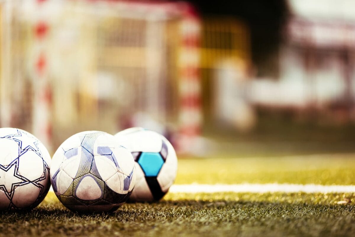 An image of Soccer balls on a green football pitch on a sunny day.